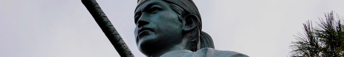 Close-up of the face of a statue of the Shinsengumi's Hijikata against a cloudy sky.