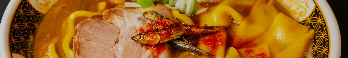 Close-up of a bowl of ramen with thick noodles, meat, green onion, and dried sardine topping.