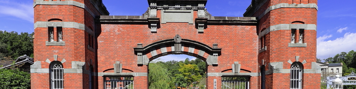 Large red brick gate with a tall tower on each side and green doors. This was the main gate of Kanazawa Prison.