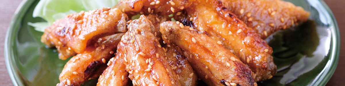 A close-up shot of fried chicken wings on a green plate. The chicken wings are covered in a light brown sauce and topped with sesame seeds.