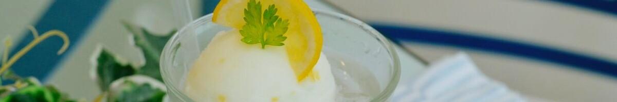 Close-up shot of vanilla ice cream scooped in a drink glass with a lemon peel and mint on top.
