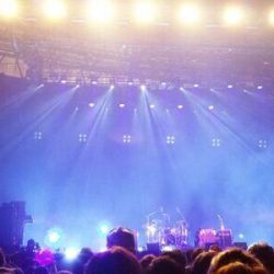 image of a live music venue stage with lights shining down from the ceiling onto the instruments, and the crowd below