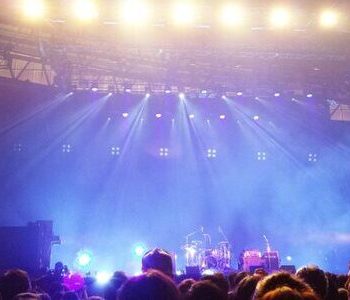 image of a live music venue stage with lights shining down from the ceiling onto the instruments, and the crowd below