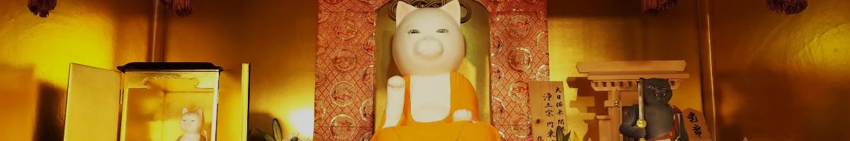 Three cat statues, one larger white one in the middle and two darker ones to the side, depicted as gods in a temple setting.