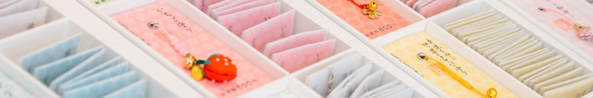 Assorted colorful envelopes alongside displays of small good-luck charms attached to cards, with charms including flowers and strawberries and bells.